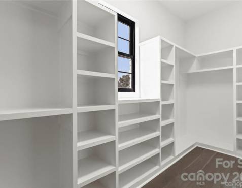 Empty white walk-in closet with multiple shelves and a window.