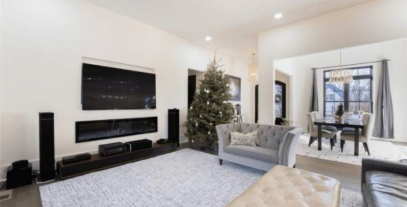 A modern living room with a mounted TV, gray sofa, and a decorated Christmas tree. A dining area with a table and chairs is visible in the background.